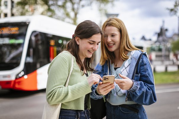 zwei junge Frauen mit Handy vor einem Bus