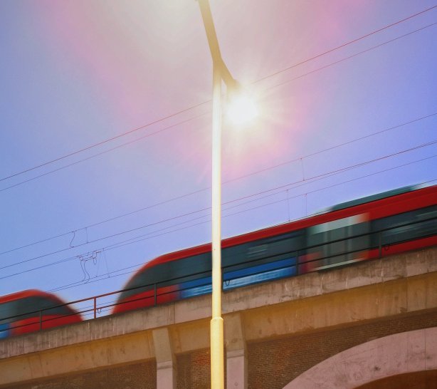 Ein roter Zug fährt bei Sonnenuntergang über ein Backsteinviadukt. Text zur Ankündigung der Auftaktveranstaltung "Revierbahn West" am 8. Juli 2025 im Rhein-Erft-Kreis, mit Logos von VRR, Go Rheinland und deutschen Ministerien.